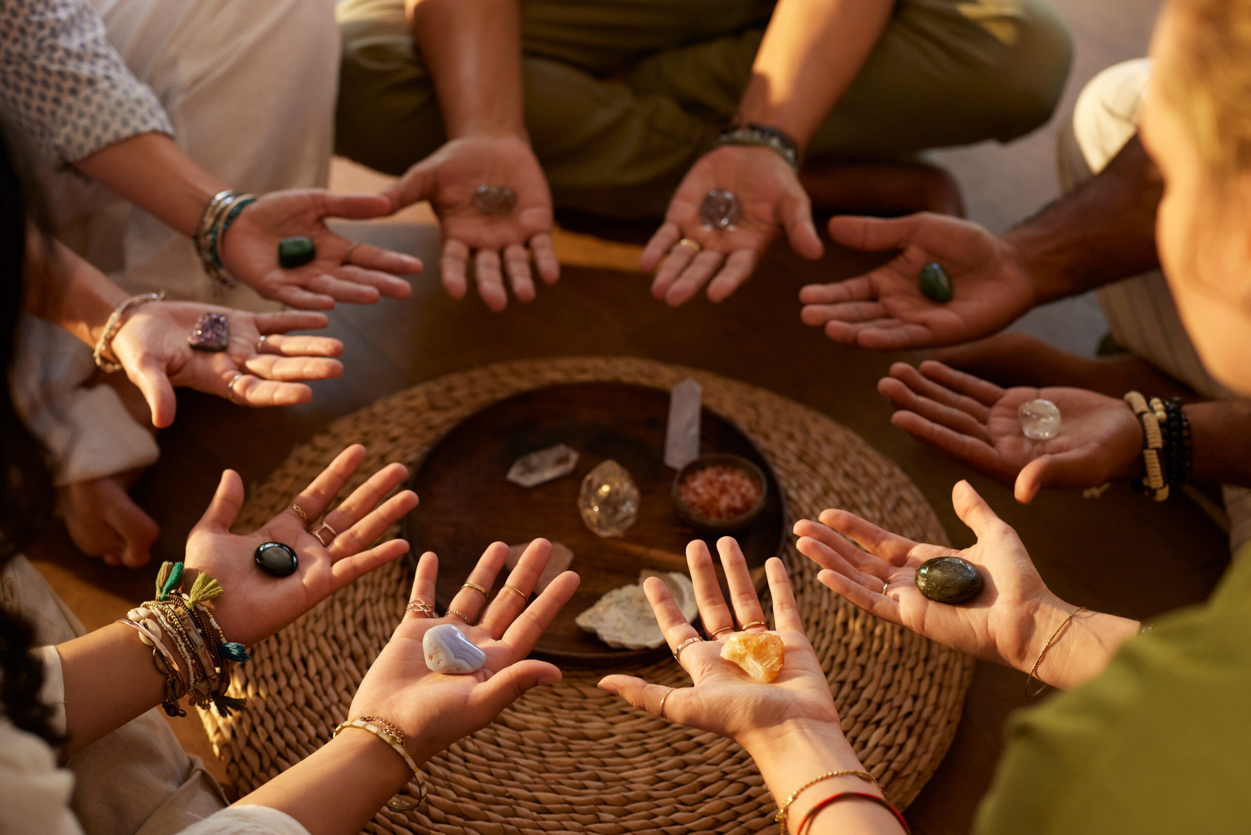 Close up of diverse group of people holding various crystals in their hands during a wellness ritual, energetical power concept. Spiritual practice with gemstones at retreat center while people sitting in circle. Rituals with gemstones for wellness, healing, meditation, destress and relaxation.